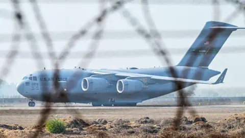 Getty Images A C-17 Globemaster III Pesawat, pesawat transportasi militer besar dengan empat mesin dan "US Air Force" Ditulis di sisi di belakang kokpit - digambarkan melalui gulungan pagar kawat berduri di Sri Guru Ram Dass Jee Bandara Internasional di Amritsar.