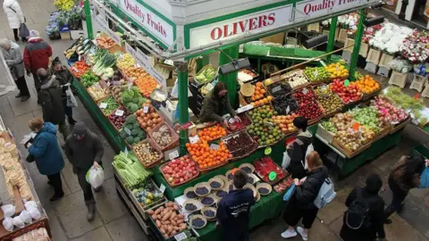 A fruit and vegetable stall in Kirkgate Market Leeds, busy with customers and full of colourful produce 