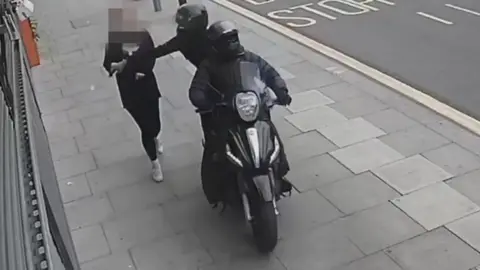A person on a moped snatching a phone out of the hands of a member of the public