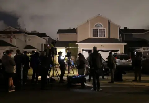 Getty Images Media crews fill the street in front of suburban homes. It's dark and you can see the silhouettes of journalists and there are bright lights of TV crews illuminating their faces.