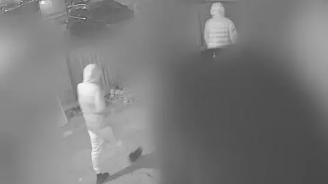 Avon and Somerset Police A black and white image showing a screenshot from the camera outside Mason's home. Most of the frame has been intentionally blurred out but you can see Max and Mason leaving the front gate of the garden and walking left down the street. 