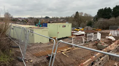 A building site with trenches dug, a number of containers on the site and fencing surrounding it