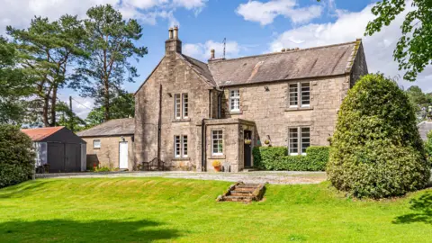 An impressive stone building with lawns and trees 