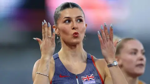 Getty Images Close-up photo of athlete Amy Hunt. Her lips are pursed together and she has her dark hair slicked back. She has an earring in each ear and has both her hands held up near to face to show off her nail art which is white nails with silver 3D balls on them. She also has a ring on one finger of each hand. She is wearing a navy blue and white striped Team GB vest and also has jewellery on both of her wrists.