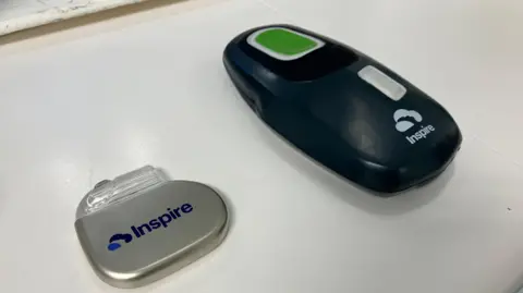 Two small devices are on a white table. One is a silver circular bit of plastic with 'inspire' written on it. The other is a larger black device which looks similar to a computer mouse. It also has 'inspire' branded on it. 
