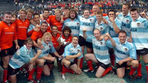 Wales players, some in red Wales shirts and some in blue and white Argentina jerseys, pose together on the pitch on the 2004 tour of Argentina.