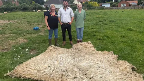 Angie, Carl and Lynn stand behind the fleece which is stretched out over the grass.