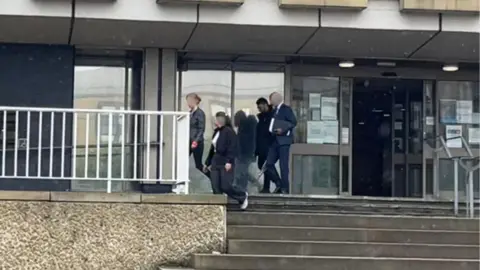 Four people walking from a court building. Three of their faces are blurred.