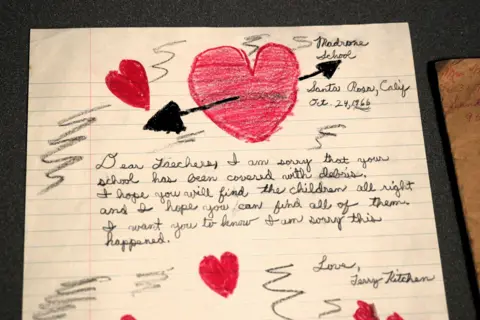 A child's handwritten letter, decorated with hearts drawn in red crayon. The text is neatly written by a child, expressing sorrow at the disaster in Aberfan and their hope that the children will be found. It is dated October 24 1966 and is sent by a child called Jenny from Madron School, Santa Rosa, California.