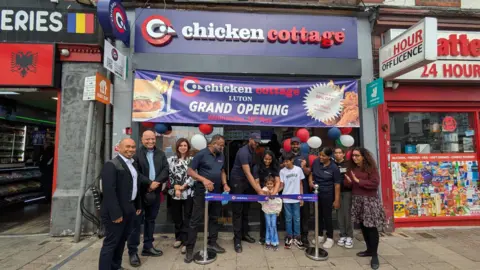 The Children's Society A group of people, some wearing uniforms for a chicken shop, and others smartly dressed, are celebrating outside a new Chicken Cottage chain