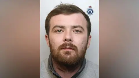 A mugshot of Sean Garner, who has a brown beard and is wearing a grey sweatshirt. 