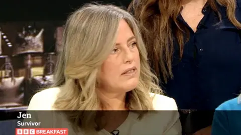 A screenshot of Jen speaking on BBC Breakfast in September. She's wearing a white jacket and is looking off-camera towards the hosts, with a serious expression on her face. The BBC Breakfast strapline describing her as "Jen, survivor" can be seen at the bottom of the screen