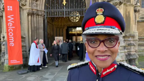 Lord lieutenant Peaches Golding is standing outside the entrance of the Bristol Cathedral in uniform.