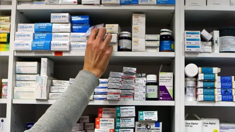 A pharmacist worker picks up a box of medication from a shelf in the store.