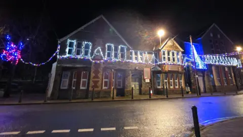 Nantyglo & Blaina town council A nighttime photo shows a long, two-storey brick building hung with Christmas lights across the top floor windows.