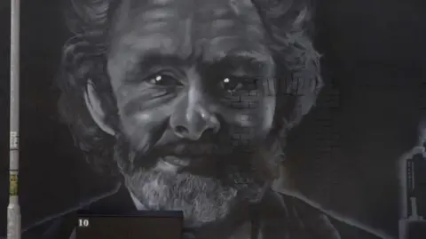 A wall with a black and white painted mural of a man with curly dark hair and a beard.