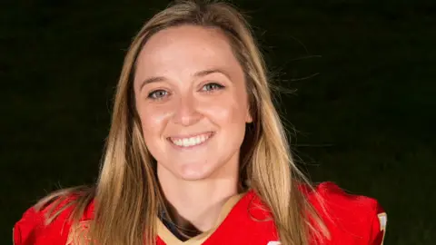 Emma Harbs A close up image of Emma Harbs, a woman in her 20s who is wearing a red sport top and has dark blonde straight hair. 