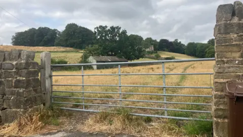 Grace Wood/BBC A metal gate between two stone walls with rolling fields behind