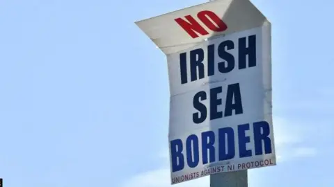 Reuters A poster on a lamp post that says 'No Irish Sea Border' and in smaller writing at the bottom it says 'Unionists against NI Protocol'. In the background is a blue sky