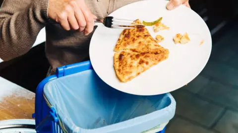 A woman throwing leftover pizza in to a bin
