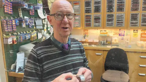 Photograph of a man who runs a watch repair business in Bolton's Crompton Place shopping centre.