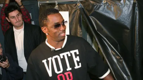 Getty Images Sean "Diddy" Combs is photographed with a voting T-shirt astatine  an lawsuit   successful  2004 urging others to ballot  successful  the election. In the background, his publicist Rob Shuter appears. 