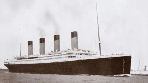 Getty Images A black and white photo of RMS Titanic, a large ocean liner with four funnels, a black hull and a white upper deck. There are masts at the front and rear.
