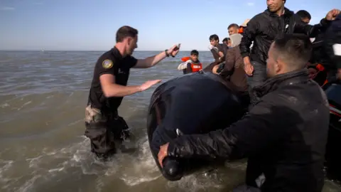 A French police officer uses a knife to slash an inflatable boat with migrants in the English Channel