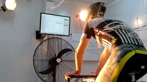 Andreas Flouris A cyclist on a static bike undergoes a test, with cables running from his helmet and shirt.