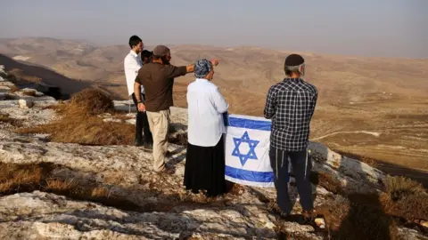 Reuters Daniella Weiss, a veteran settler leader, holds an Israeli flag during a scouting mission to find new hilltops to settle near the Israeli settlement of Kokhav Hashahar, in the occupied West Bank (6 November 2022)