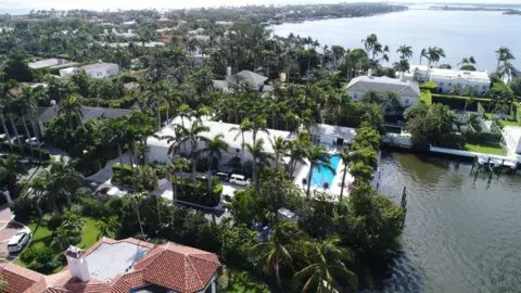 Miami Herald via Getty News An aerial view of Jeffrey Epstein's home in Palm Beach, showing a large white house in a waterfront neighbourhood, with a pool visible among many palm trees.
