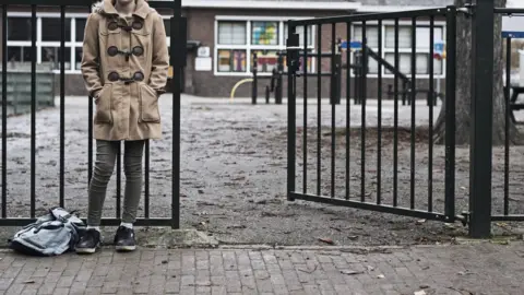 Getty Images Child waiting at the school playground gates