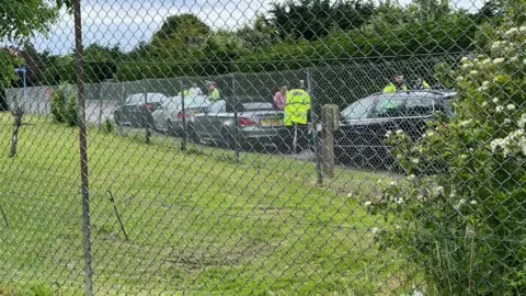Andrew Turner/BBC Cars pulled over by police with drivers being interviewed, with a fence partially obscuring the view