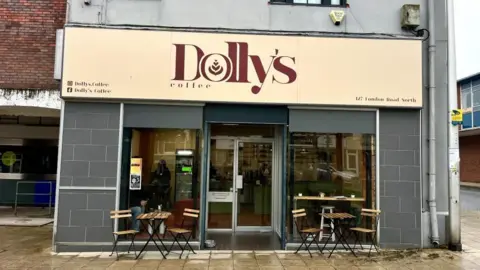 Martin Giles/BBC The outside of Dolly's coffee shop, there are chairs and tables. The front of the shop is glass and the shop signage says "Dolly's". 