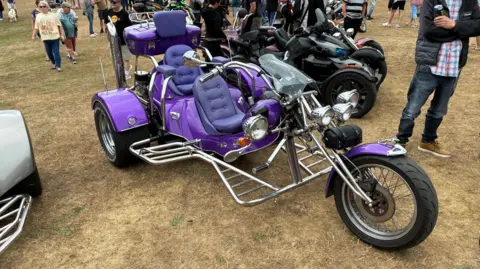 A three-wheeled purple motorcycle parked on a grass field. 