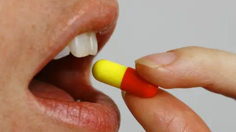 PA Media The open mouth of a female who is about to take a red and yellow capsule which is held between their thumb and forefinger.