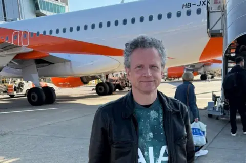Michael Green Michael Green wearing a bluey-green Spurs on the runway in front of an orange and white plane