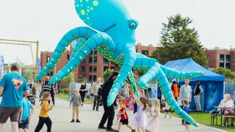 Young children play near a large inflatable bluey green octopus, with a blue tent in the background at last year's festival.