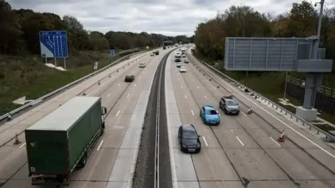 Looking down on the motorway from a bridge as traffic passes by underneath.