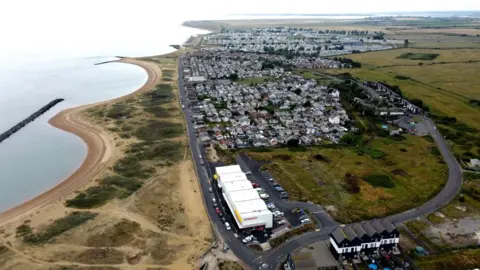 A bird's eye view of a seaside village with houses, the coast and the sea visible
