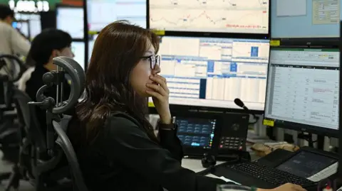 A currency dealer has her hand over her mouth as she and her team monitor exchange rates in a dealing room at the Hana Bank headquarters in Seoul on 4 March 