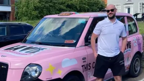 Brian Farmer/BBC Matthew Murphy standing next to pink taxi