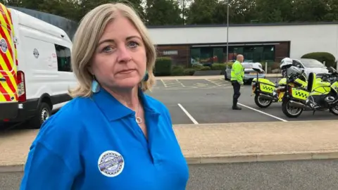 James Grant/BBC A woman in a blue polo stands in front of a police van. 