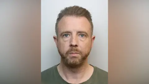 Police mugshot of Alan Styles. He is wearing a green T-shirt and he has short ginger hair and a short ginger beard. He has a nose ring.