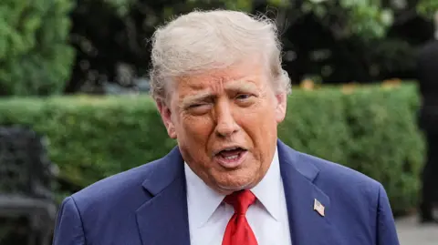Donald Trump speaks while wearing a blue suit, white shirt and red tie.