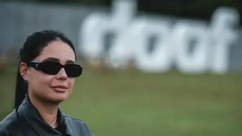 DJ Hannah Laing organises, headlines and sells out debut Doof festival 1 BBC Hannah Laing, in dark sunglasses, her dark hair in a ponytail and wearing a black leather jacket, stands with a large "Doof" sign behind her in Camperdown Park