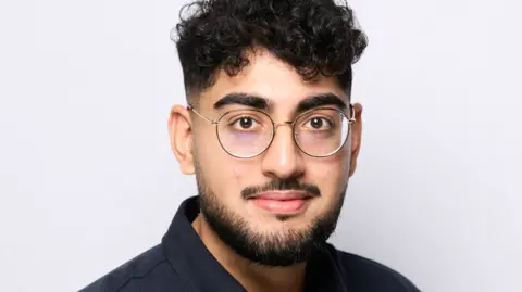 Image of Pavan Bhatt, a man with short dark curly hair and glasses wearing a black shirt and standing in front of a white background