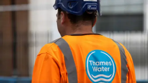 Getty Images Bagian belakang pekerja air Thames yang mengenakan atasan hi-vis oranye dengan topi keras konstruksi biru