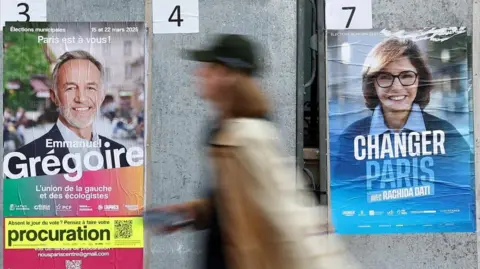 A woman walks past electoral posters of Emmanuel Grégoire and Rachida Dati in Paris.