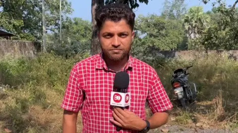 Bastar Junction Mukesh Chandrakar, wearing a red and white check shirt, holds a microphone as he talks to camera during a video filmed for his YouTube channel last month